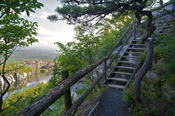 A branch of one of many hiking trails leading up to a gazebo seen against guest rooms in the far background across Lake Mohonk at Mohonk Mountain House