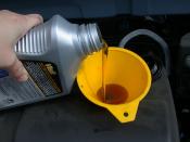Using a funnel to refill the motor oil in an automobile as part of an oil change.