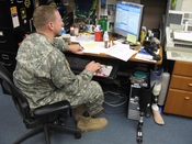 English: Major David Rozelle works at his desk next to his extra prosthesis. He keeps them there so he can switch them out, depending on his activity. He uses one to run, one to bike and one with a boot with his uniform. As deputy to the program manager f
