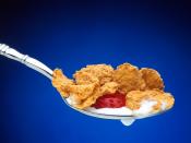 A spoon containing breakfast cereal flakes, part of a strawberry, and milk is held in midair against a blue background.