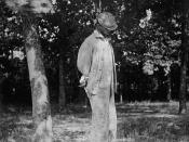 A man lynched from a tree. Face partially concealed by angle and headgear.