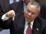 English: At the UN, Colin Powell holds a model vial of anthrax, while arguing that Iraq is likely to possess WMDs.