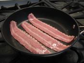 Three strips of Oscar Mayer brand turkey bacon cooking in a skillet.