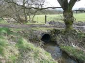 English: Culvert under field access, Glovershaw, Bingley The modern way to bridge a stream; stone and soil over a large plastic pipe, corrugated for extra strength.
