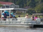 A pontoon boat approaches on Lake Gaston, VA-NC with choir and friends from Genesis UMC of Cary, North Carolina. Two rafts sit on the back of the boat above the engine. Photo by James E. Scarborough July 10, 2004.