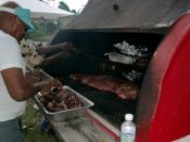 English: A barbecue on a trailer at a block party in Kansas City. Pans on the top shelf hold hamburgers and hot dogs that were grilled earlier when the coals were hot. The lower grill is now being used to slowly cook pork ribs and 
