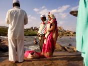 A Muslim couple being wed alongside the Tungabhadra River at Hampi, India. In the background, a Hindu man is taking his ritual bath.