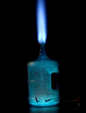 English: Combustion of an ethanol vapour + air mixture in a water cooler bottle. Visible at the bottom of the image are the ignition leads. The top of the image shows a blast of light blue flame which has dislodged a soft toy ball from the neck of the bot