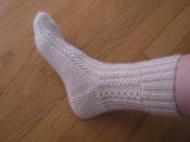 A hand knitted white lace sock award for generosity made out of handspun wool- a blend of Cotswold and mutt.