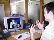 English: A Deaf, Hard-Of-Hearing or Speech-Impaired person at his workplace, communicating with a hearing person via a Video Relay Service video interpreter (a V.I., a Sign Language interpreter, shown on-screen), using a videophone. The hearing person wit