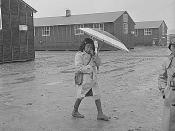 Jerome Relocation Center, Denson, Arkansas. The Arkansas rainy season, and this young resident of the Jerome Center dons rubber boots and carries a parasol. The (buckshot) mud makes the trip to and from school a little dificult. (Japanese American interme