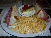 Montreal Style Smoked meat Sandwich on rye bread with swiss cheese and cole slaw and french fries.