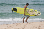 A surfer carries a surfboard along the beach