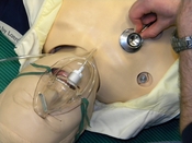 English: Auscultation of lungs / Auscultation of pulmonary sounds / Auscultation of breath sounds /Auscultation of respiratory sounds of a doll with a stethoscope in an out-of-hospital exercise. The oxygen mask seems to be sligtly oversized...