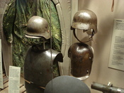 English: WWI German body armor, double-reinforced steel helmet, and arm shield on display at the Canadian War Museum with WWI sniper camouflage in background.