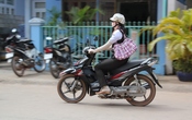 English: A woman riding a motorcycle in Dương Đông, Phú Quốc, South Vietnam. She wears long gloves and a hat to protect her skin from the sun, despite the heat (around 30°C).